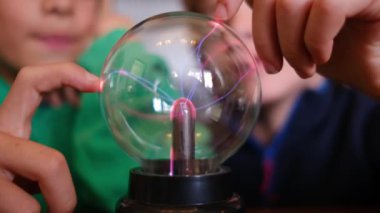 Küçük çocuklar masada yıldırımla plazma topu çalışıyor.