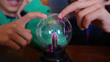 Küçük çocuklar masada yıldırımla plazma topu çalışıyor.