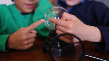 Küçük çocuklar masada yıldırımla plazma topu çalışıyor.