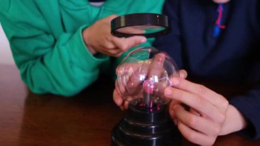 Küçük çocuklar masada yıldırımla plazma topu çalışıyor.