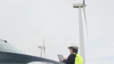 Arabanın yanındaki kadın elektrik mühendisi telsizle konuşuyor, dijital tablet kullanıyor ve rüzgar türbinlerini kontrol ediyor.