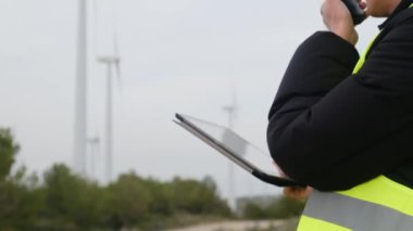 Rüzgar türbinlerini kontrol ederken telsiz ve dijital tablet kullanan kadın elektrik mühendisi
