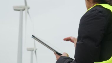 Rüzgar türbinlerini kontrol ederken telsiz ve dijital tablet kullanan kadın elektrik mühendisi