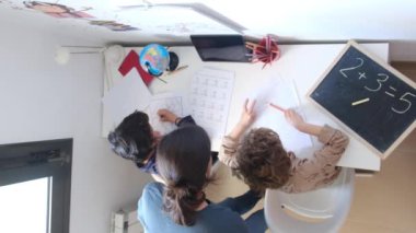 Anne, oğullarına evde matematik ödevi yaparken yardım ediyor.