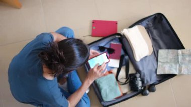 Seyahatten önce bavulda eşya toplarken akıllı telefon kullanan kadın yolcuların en üst görüntüsü