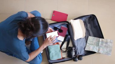 Seyahatten önce bavulda eşya toplarken akıllı telefon kullanan kadın yolcuların en üst görüntüsü