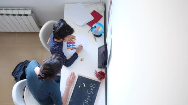自宅でテーブルで数学の宿題をする彼女の息子を助ける母親のトップビュー — ストック動画