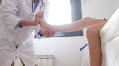 Kadın doktor klinikte erkek hastanın kırık bacağına masaj yapıyor.