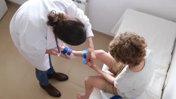 Kobieta Lekarz Zakładając Ortezę Derotacji Złamanie Nogi Chłopca Klinice — Wideo stockowe