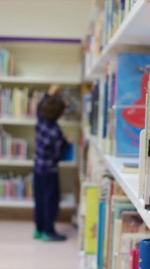 Küçük çocuk kütüphanede kitap seçiyor.