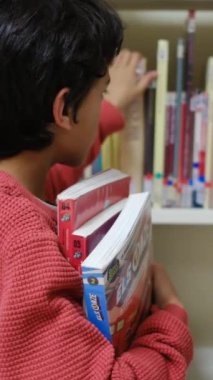 Küçük çocuk kütüphanede kitap seçiyor.