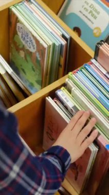 Küçük çocuk kütüphanede kitap seçiyor.