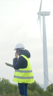Kadın elektrik, mühendis telsizle konuşuyor, dijital tablet kullanıyor ve rüzgar türbinini kontrol ediyor.
