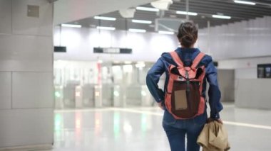 Sırt çantalı genç bir kadın metroda turnikelere doğru yürüyor..