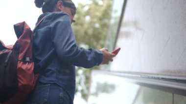 Yürüyen merdivende akıllı telefonu olan genç bir kadın. 