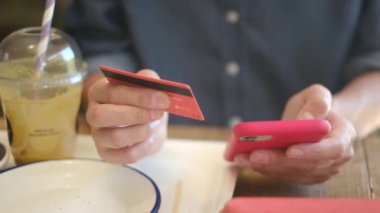 Kafede akıllı telefon ve kredi kartıyla internetten alışveriş yapan genç bir kadın. 