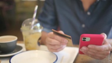 Kafede akıllı telefon ve kredi kartıyla internetten alışveriş yapan genç bir kadın. 