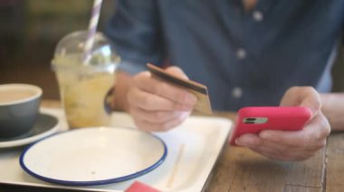 Kafede akıllı telefon ve kredi kartıyla internetten alışveriş yapan genç bir kadın. 