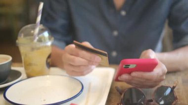 Kafede akıllı telefon ve kredi kartıyla internetten alışveriş yapan genç bir kadın. 