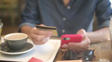 Kafede akıllı telefon ve kredi kartıyla internetten alışveriş yapan genç bir kadın. 