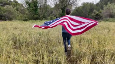 Amerika bayrağıyla sahada koşan bir kadının arka plan görüntüsü. 4 Temmuz Bağımsızlık Günü.