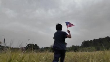 Amerika bayrağı elinde koşan bir çocuğun arka görüntüsü. 4 Temmuz Bağımsızlık Günü.