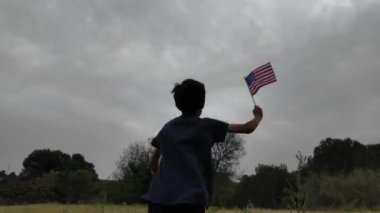 Amerika bayrağı elinde koşan bir çocuğun arka görüntüsü. 4 Temmuz Bağımsızlık Günü.