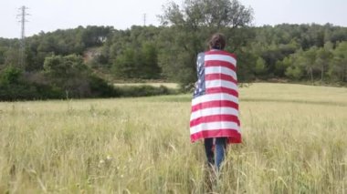 ABD bayraklı bir kadının tarlada yürüyüşü. 4 Temmuz Bağımsızlık Günü.