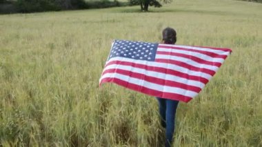 ABD bayraklı bir kadının tarlada yürüyüşü. 4 Temmuz Bağımsızlık Günü.