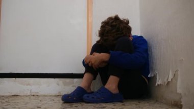 Üzgün çocuk eski püskü duvarın yanında dizlerinin üzerinde oturuyor.