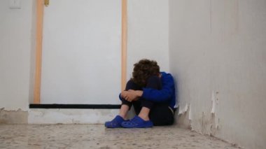Üzgün çocuk eski püskü duvarın yanında dizlerinin üzerinde oturuyor.