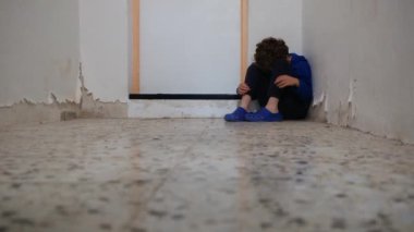 Üzgün çocuk eski püskü duvarın yanında dizlerinin üzerinde oturuyor.