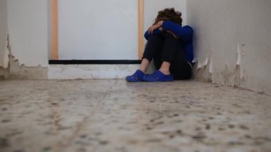 Üzgün çocuk eski püskü duvarın yanında dizlerinin üzerinde oturuyor.