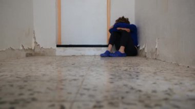 Üzgün çocuk eski püskü duvarın yanında dizlerinin üzerinde oturuyor.