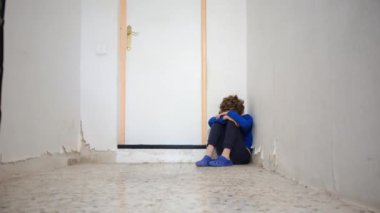 Üzgün çocuk eski püskü duvarın yanında dizlerinin üzerinde oturuyor.