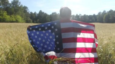 Buğday tarlasında Amerikan bayrağı taşıyan bir çocuğun arka görüntüsü. 4 Temmuz Bağımsızlık Günü.