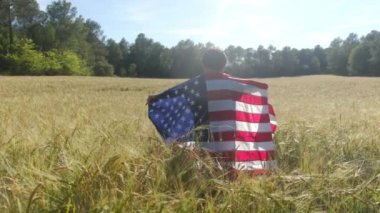 Buğday tarlasında Amerikan bayrağı taşıyan bir çocuğun arka görüntüsü. 4 Temmuz Bağımsızlık Günü.