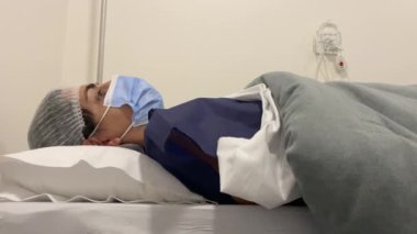 Yüzü maskeli hasta hastanede yatağında yatıyor.