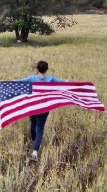 Amerika bayrağıyla sahada koşan bir kadının arka plan görüntüsü. 4 Temmuz Bağımsızlık Günü.