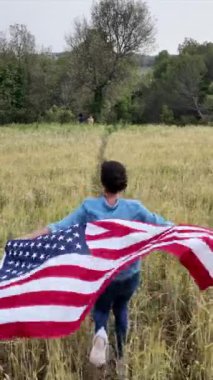 Amerika bayrağıyla sahada koşan bir kadının arka plan görüntüsü. 4 Temmuz Bağımsızlık Günü.