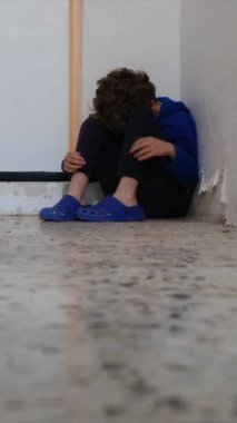 Üzgün çocuk eski püskü duvarın yanında dizlerinin üzerinde oturuyor.