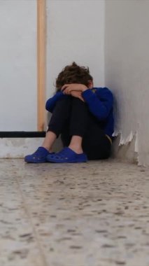 Üzgün çocuk eski püskü duvarın yanında dizlerinin üzerinde oturuyor.