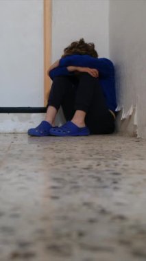 Üzgün çocuk eski püskü duvarın yanında dizlerinin üzerinde oturuyor.