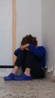 Üzgün çocuk eski püskü duvarın yanında dizlerinin üzerinde oturuyor.
