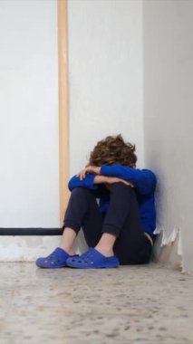 Üzgün çocuk eski püskü duvarın yanında dizlerinin üzerinde oturuyor.