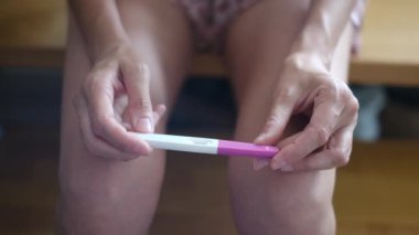 Hamilelik testi olan genç bir kadın, sonuçları kontrol ediyor, sabahları evde oturuyor. Hamilelik, sağlık