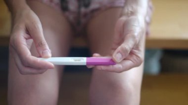 Hamilelik testi olan genç bir kadın, sonuçları kontrol ediyor, sabahları evde oturuyor. Hamilelik, sağlık