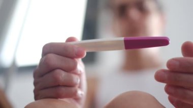 Hamilelik testi olan genç bir kadın, sonuçları kontrol ediyor, sabahları evde oturuyor. Hamilelik, sağlık