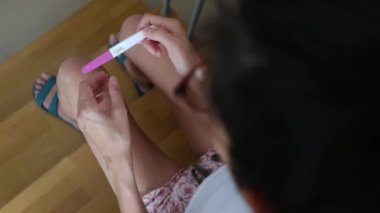 Hamilelik testi olan genç bir kadın, sonuçları kontrol ediyor, sabahları evde oturuyor. Hamilelik, sağlık