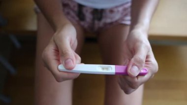 Hamilelik testi olan genç bir kadın, sonuçları kontrol ediyor, sabahları evde oturuyor. Hamilelik, sağlık